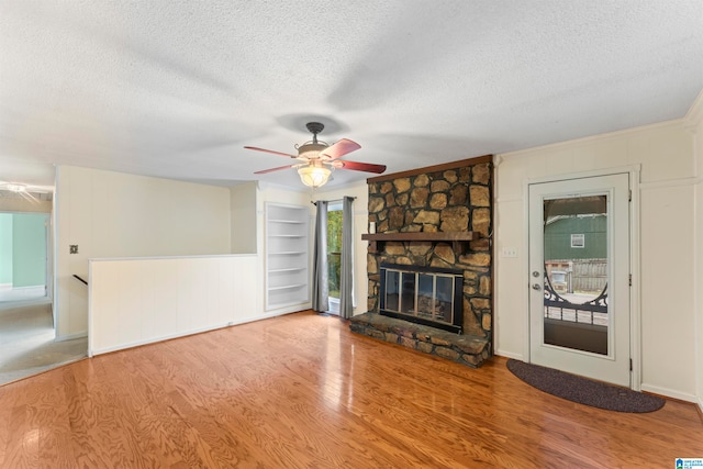 unfurnished living room with a textured ceiling, hardwood / wood-style flooring, and a stone fireplace