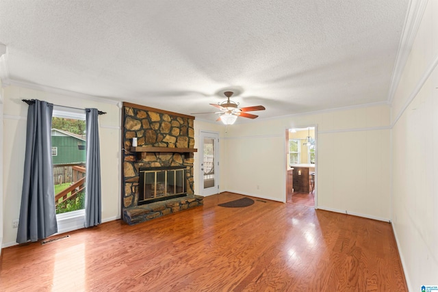 unfurnished living room featuring a stone fireplace, wood-type flooring, crown molding, and a textured ceiling