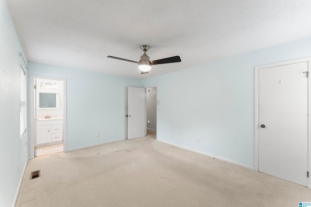 unfurnished bedroom with ceiling fan, ensuite bathroom, light carpet, and a textured ceiling