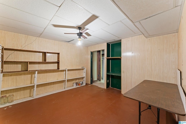 basement featuring wood walls, a drop ceiling, and ceiling fan