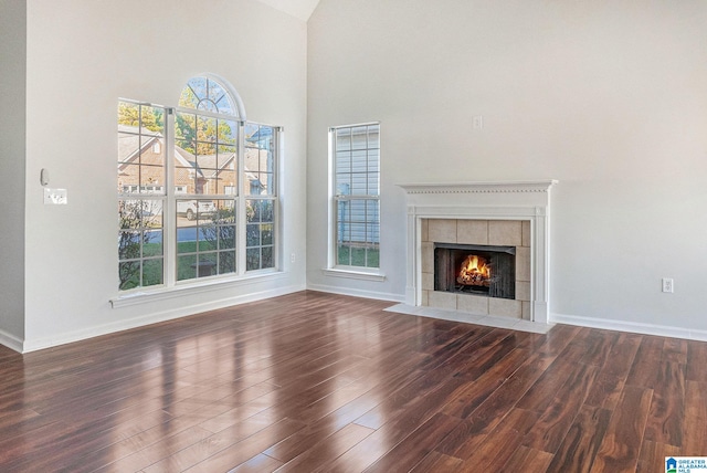 unfurnished living room featuring dark hardwood / wood-style flooring, a towering ceiling, and a tile fireplace