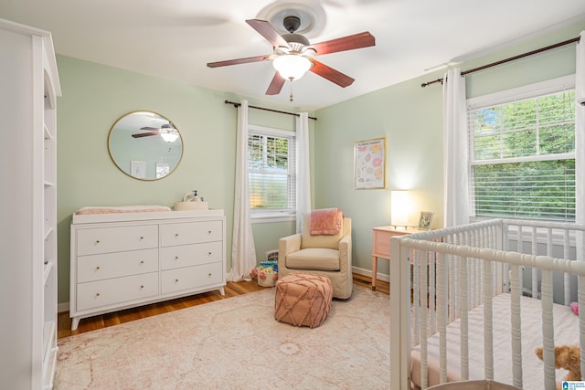 bedroom with a nursery area, ceiling fan, and light hardwood / wood-style flooring