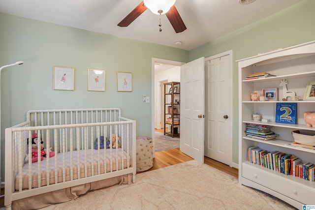 bedroom with a closet, a nursery area, hardwood / wood-style flooring, and ceiling fan