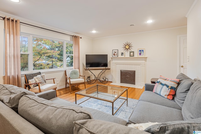 living room featuring wood-type flooring, a tile fireplace, and ornamental molding