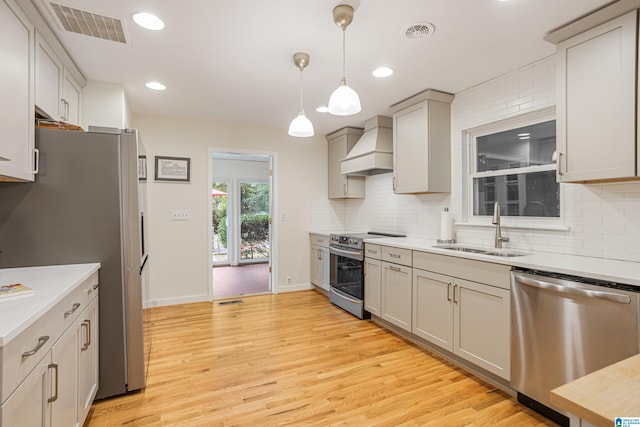 kitchen featuring light wood-type flooring, appliances with stainless steel finishes, hanging light fixtures, sink, and custom exhaust hood