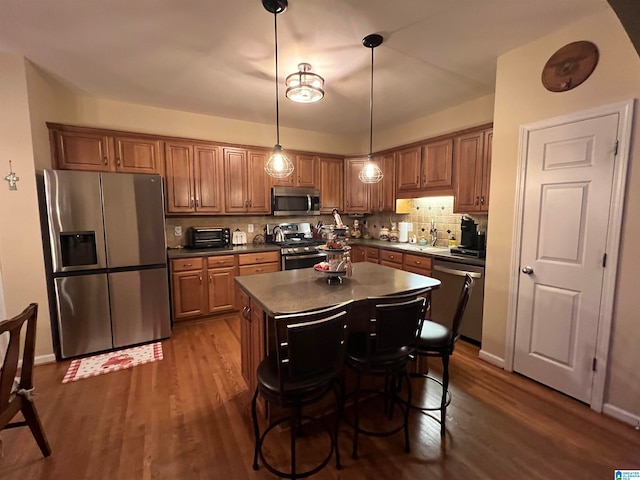 kitchen with pendant lighting, stainless steel appliances, tasteful backsplash, a kitchen island, and dark hardwood / wood-style flooring