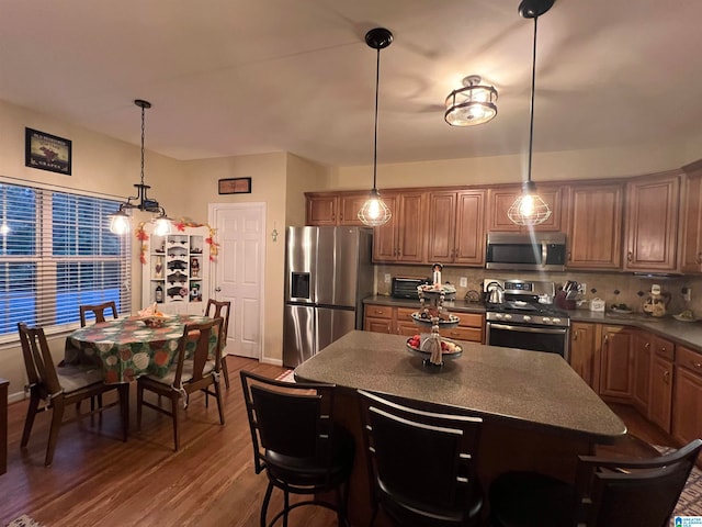 kitchen with stainless steel appliances, decorative light fixtures, dark hardwood / wood-style flooring, and backsplash