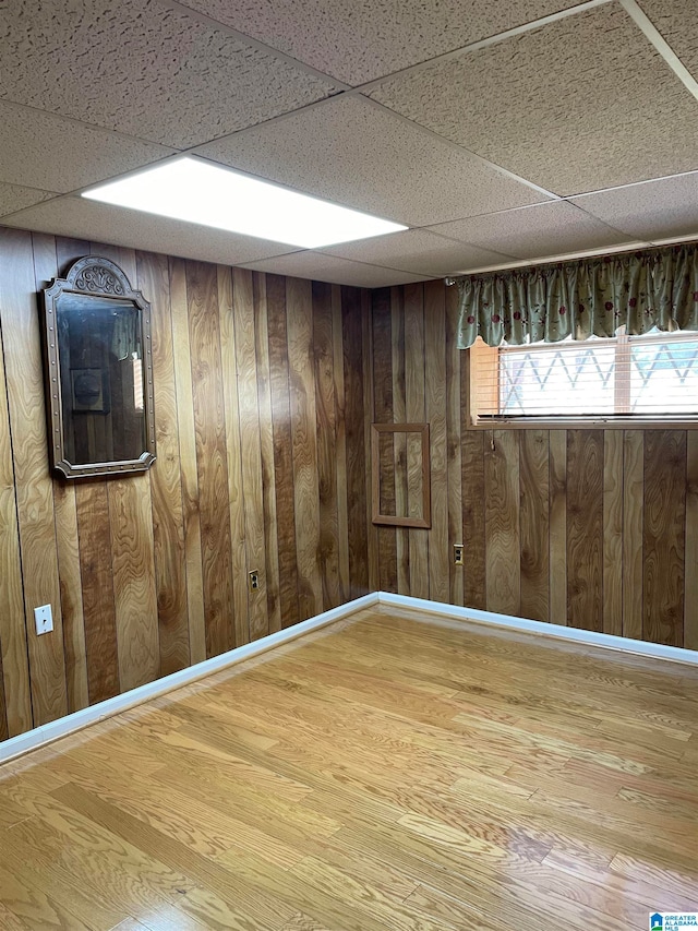 basement with hardwood / wood-style floors, wood walls, and a drop ceiling