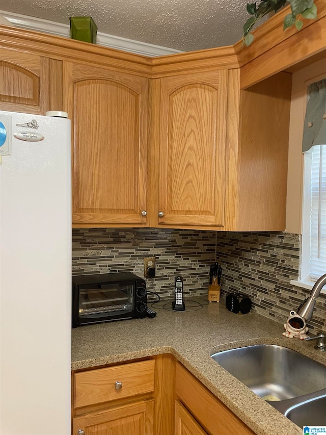 kitchen with a textured ceiling, white fridge, backsplash, and sink