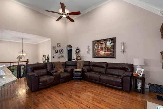 living room featuring a towering ceiling, wood-type flooring, ceiling fan with notable chandelier, and crown molding