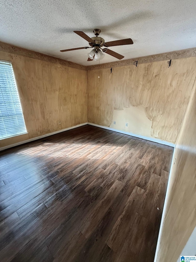 unfurnished room featuring dark wood-type flooring, ceiling fan, a textured ceiling, and wood walls