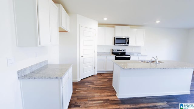 kitchen with appliances with stainless steel finishes, dark hardwood / wood-style flooring, sink, white cabinets, and a kitchen island with sink