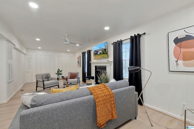 living room with a fireplace, light hardwood / wood-style flooring, ceiling fan, and crown molding