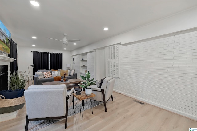 living room with ceiling fan, light hardwood / wood-style floors, and brick wall