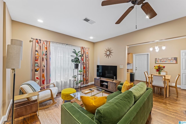 living room with ceiling fan with notable chandelier and light hardwood / wood-style floors