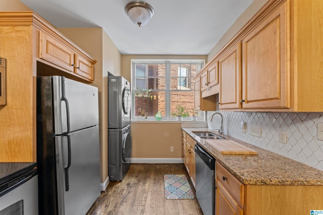 kitchen with appliances with stainless steel finishes, light stone counters, sink, hardwood / wood-style flooring, and stacked washer / dryer