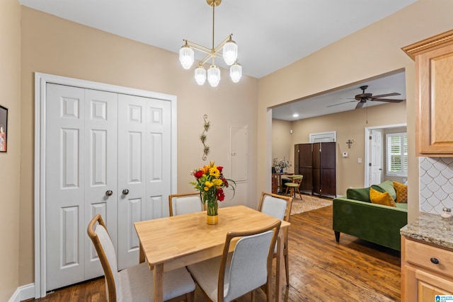 dining area with ceiling fan with notable chandelier and dark hardwood / wood-style flooring