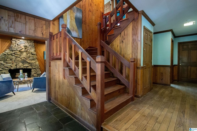 staircase with a fireplace, wood-type flooring, crown molding, and wooden walls