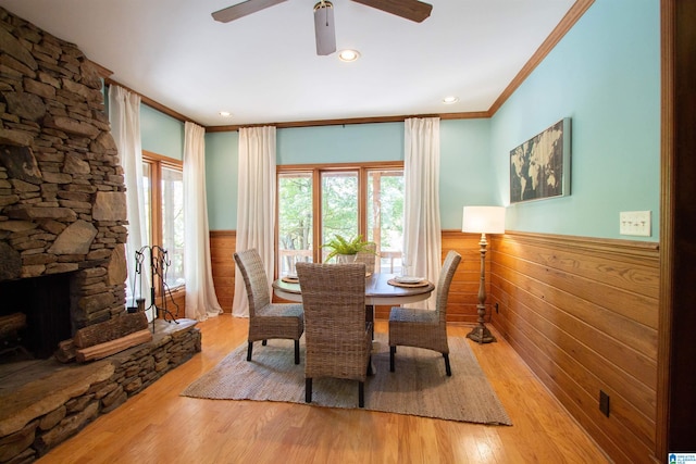 dining space with light wood-type flooring, a stone fireplace, ceiling fan, and crown molding