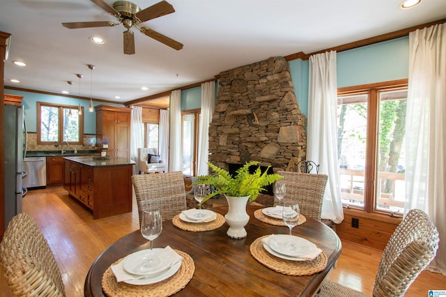 dining room with a stone fireplace, sink, a healthy amount of sunlight, and light hardwood / wood-style floors