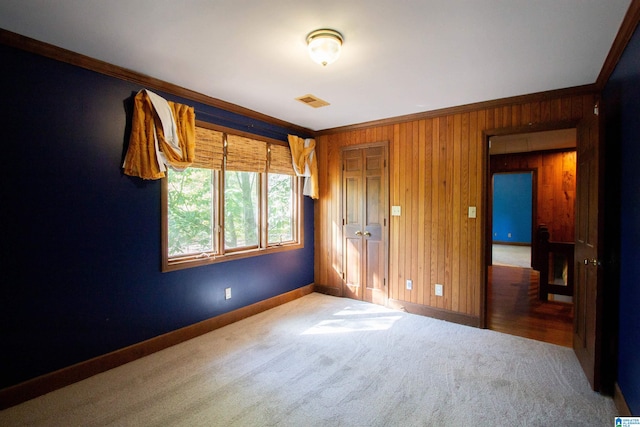 unfurnished bedroom with carpet flooring, crown molding, wooden walls, and a closet