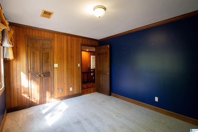 unfurnished bedroom with wood walls, a closet, carpet floors, and ornamental molding