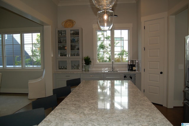 kitchen featuring hanging light fixtures, light stone counters, a healthy amount of sunlight, and white cabinets