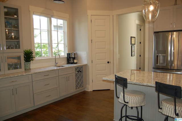 kitchen featuring dark hardwood / wood-style floors, light stone countertops, stainless steel refrigerator with ice dispenser, sink, and white cabinets