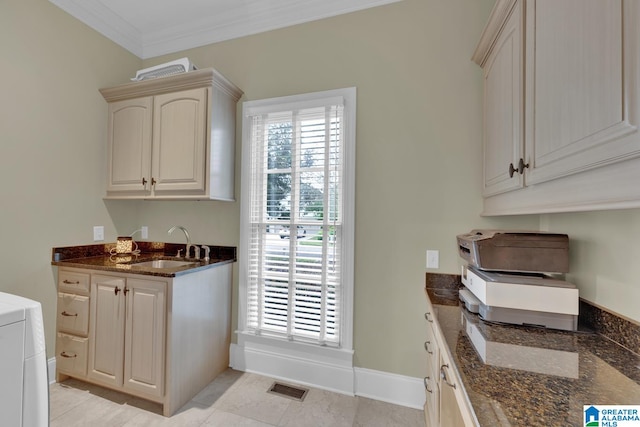 interior space featuring light tile patterned flooring, sink, dark stone countertops, washer / clothes dryer, and crown molding