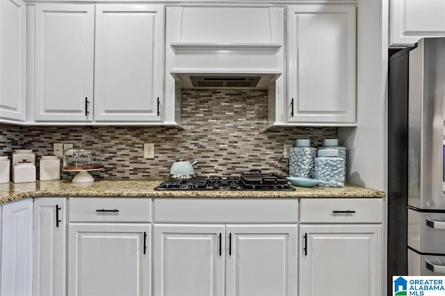 kitchen featuring white cabinets, custom range hood, stainless steel refrigerator, and black gas cooktop