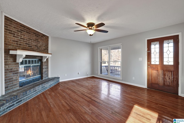 unfurnished living room with a textured ceiling, ceiling fan, dark wood-type flooring, and a brick fireplace