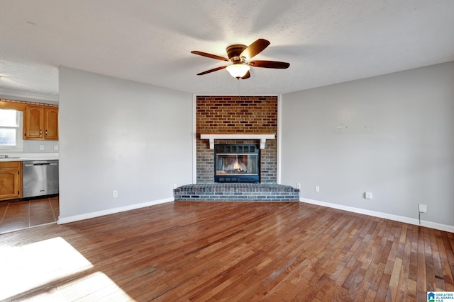 unfurnished living room featuring ceiling fan, a fireplace, wood-type flooring, and a textured ceiling