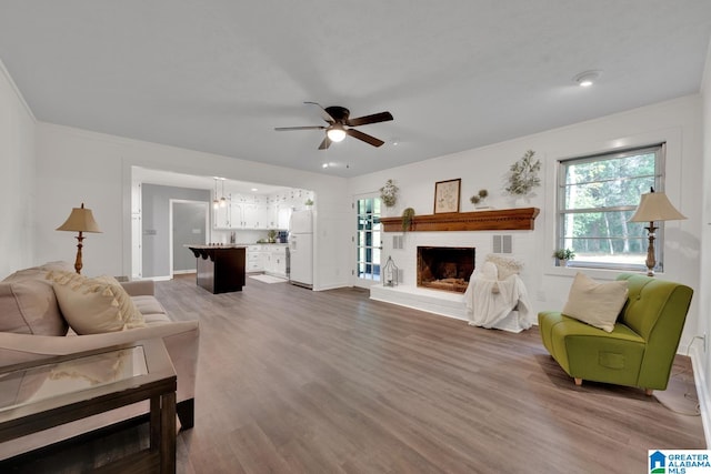 living room featuring a brick fireplace, hardwood / wood-style flooring, ceiling fan, and crown molding