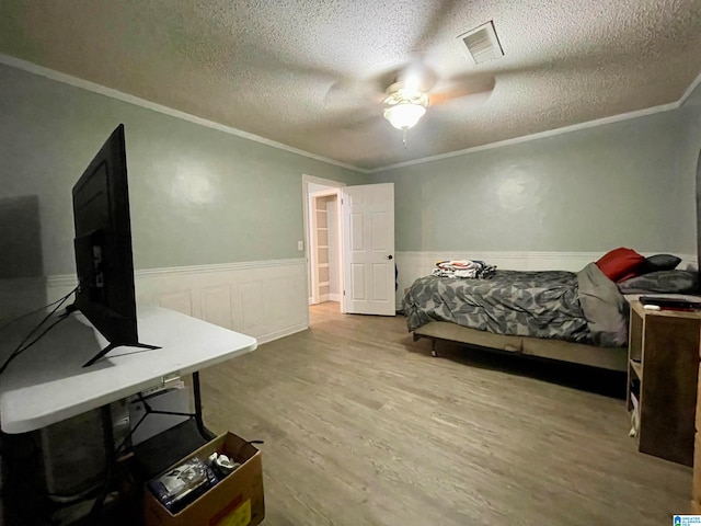 bedroom with ceiling fan, a textured ceiling, light hardwood / wood-style flooring, and crown molding