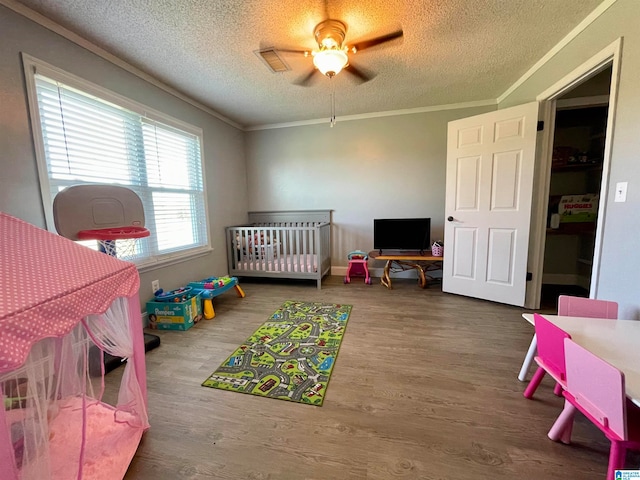 bedroom with ceiling fan, a crib, wood-type flooring, and a textured ceiling