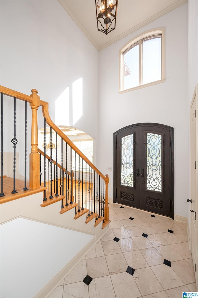 entryway featuring french doors, a towering ceiling, ornamental molding, light tile patterned floors, and a chandelier