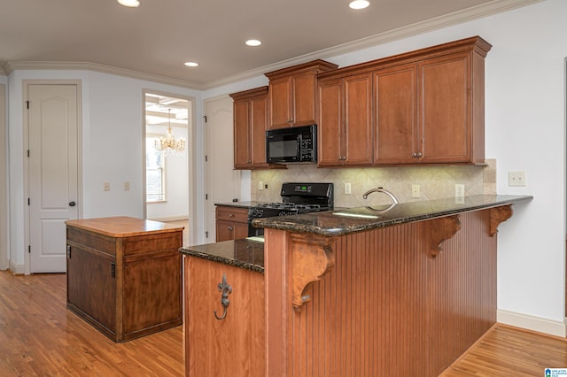 kitchen featuring kitchen peninsula, a breakfast bar, crown molding, black appliances, and dark stone countertops