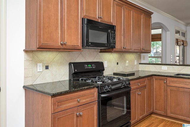 kitchen featuring ornamental molding, light hardwood / wood-style flooring, dark stone countertops, and black appliances