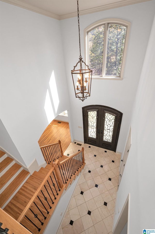 foyer with tile patterned floors, crown molding, french doors, and a chandelier