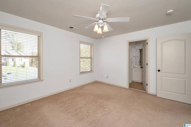 unfurnished bedroom featuring ceiling fan, light carpet, and ensuite bath