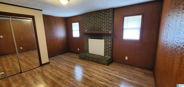 unfurnished living room with a fireplace, wooden walls, a textured ceiling, and hardwood / wood-style floors