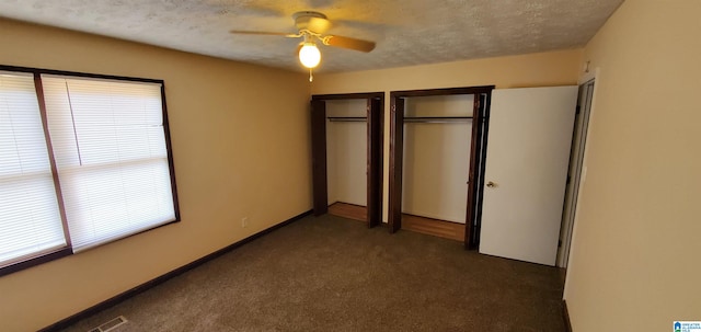 unfurnished bedroom featuring two closets, dark carpet, ceiling fan, and a textured ceiling