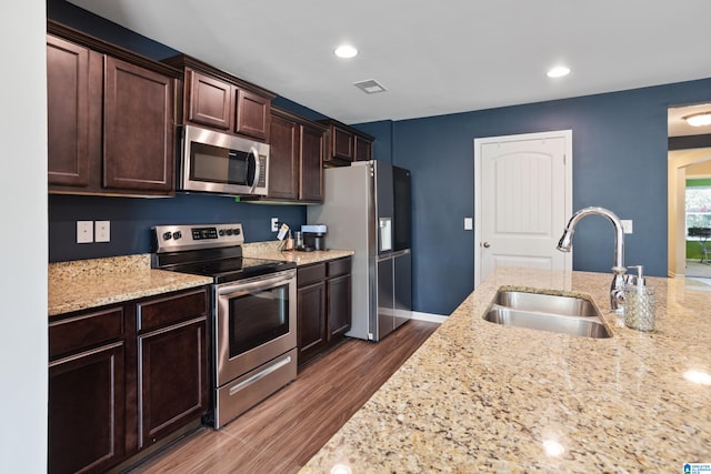 kitchen featuring stainless steel appliances, dark brown cabinets, dark hardwood / wood-style flooring, light stone countertops, and sink