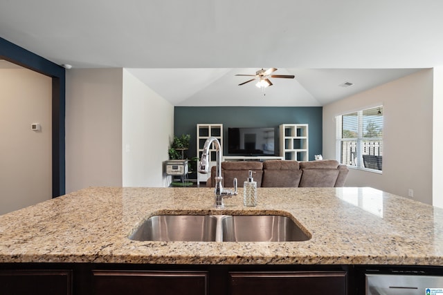 kitchen featuring lofted ceiling, light stone counters, sink, stainless steel dishwasher, and ceiling fan