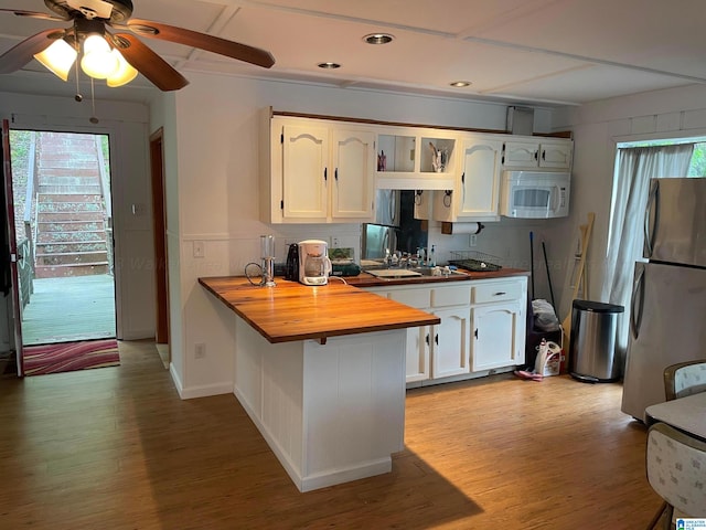 kitchen with white cabinets, kitchen peninsula, butcher block countertops, stainless steel refrigerator, and light hardwood / wood-style flooring