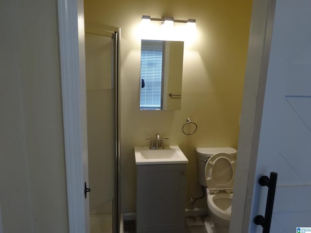 bathroom featuring a shower with door, vanity, and toilet