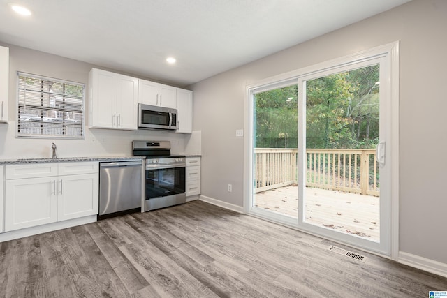 kitchen with light hardwood / wood-style flooring, white cabinetry, sink, appliances with stainless steel finishes, and light stone counters