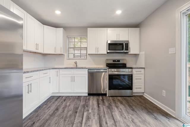 kitchen with white cabinets, dark hardwood / wood-style flooring, stainless steel appliances, and light stone countertops