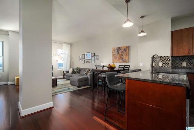 kitchen featuring decorative light fixtures, dark hardwood / wood-style flooring, decorative backsplash, sink, and dark stone countertops