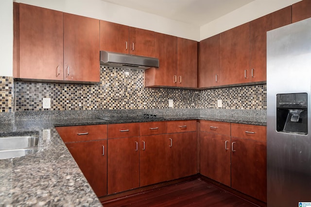 kitchen featuring dark stone counters, stainless steel refrigerator with ice dispenser, dark hardwood / wood-style floors, backsplash, and black stovetop